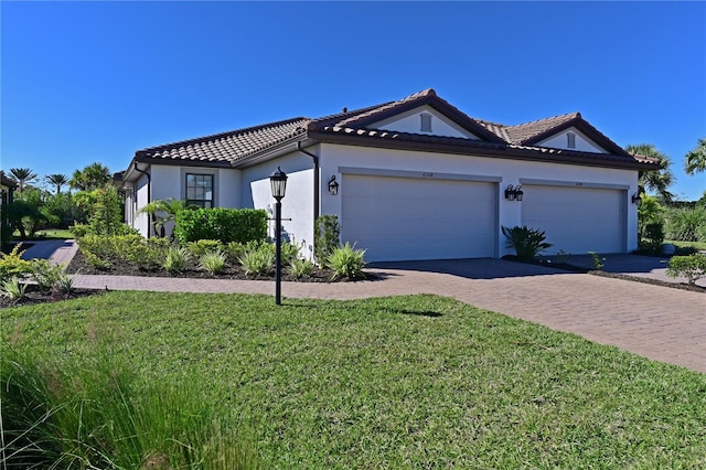 view of front facade featuring an attached garage, a tile roof, stucco siding, a front lawn, and driveway