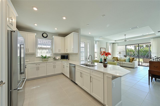 kitchen featuring open floor plan, a peninsula, light countertops, appliances with stainless steel finishes, and a sink