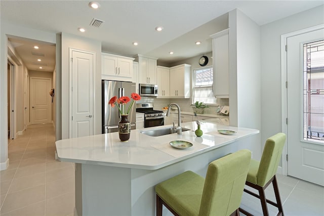 kitchen with a peninsula, light tile patterned floors, decorative backsplash, stainless steel appliances, and a sink