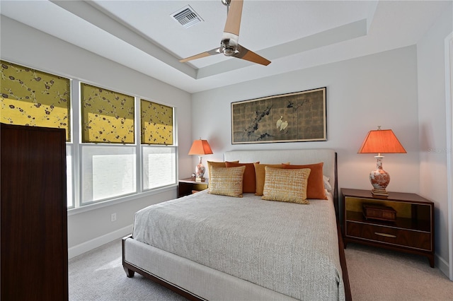 carpeted bedroom featuring visible vents, baseboards, a raised ceiling, and a ceiling fan