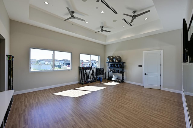 workout room featuring a tray ceiling, wood finished floors, and ceiling fan