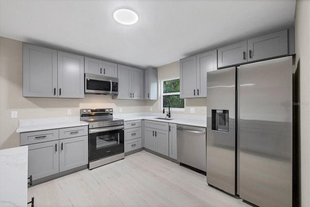 kitchen with light wood-type flooring, light countertops, gray cabinets, a sink, and stainless steel appliances