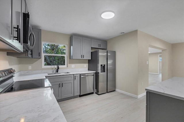 kitchen featuring light wood-style floors, a sink, gray cabinetry, and stainless steel appliances