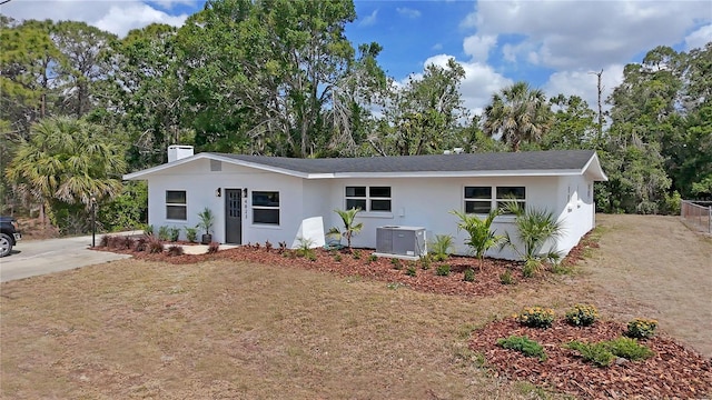 ranch-style house featuring a chimney, driveway, central AC unit, and stucco siding