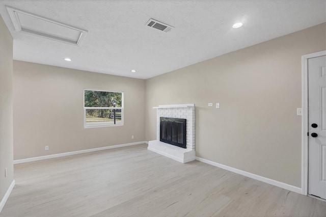 unfurnished living room with visible vents, a brick fireplace, baseboards, attic access, and light wood-style flooring