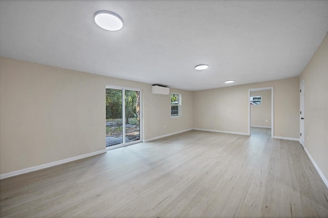 unfurnished room featuring baseboards, a wall unit AC, and light wood-type flooring