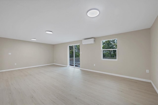 unfurnished room featuring baseboards, a wall mounted AC, and light wood-type flooring