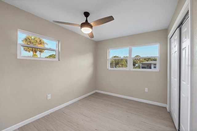 unfurnished bedroom with a closet, baseboards, multiple windows, and light wood-type flooring