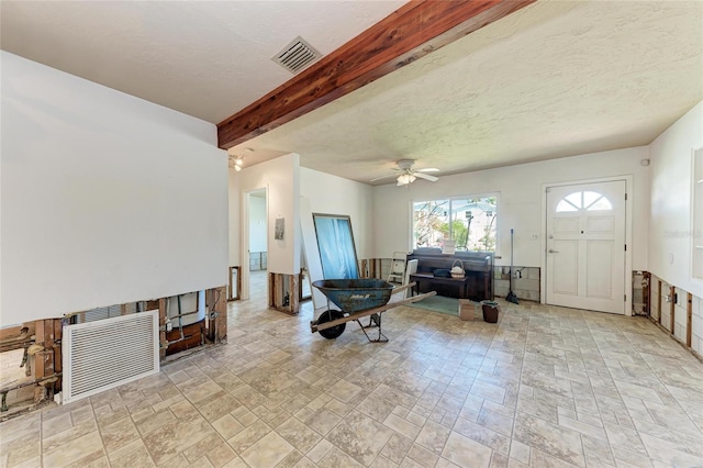 living area featuring a textured ceiling, a ceiling fan, stone finish floor, visible vents, and beamed ceiling
