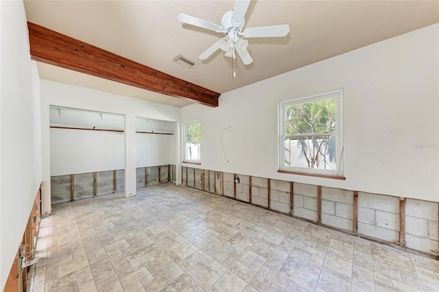 spare room with beamed ceiling, a ceiling fan, and a wealth of natural light