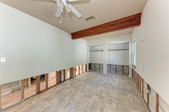 empty room featuring stone finish flooring, visible vents, beamed ceiling, and a ceiling fan