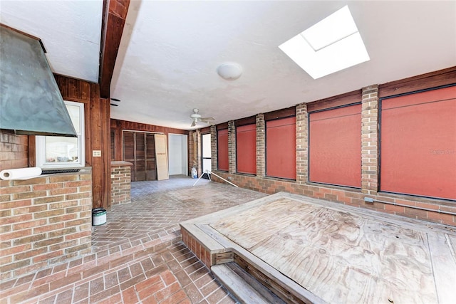 interior space featuring brick floor, ceiling fan, and a skylight