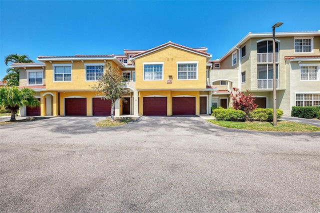 multi unit property with an attached garage, a tile roof, driveway, and stucco siding