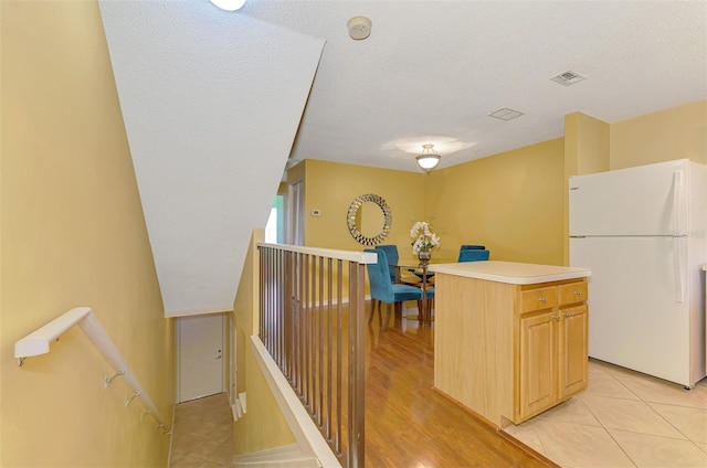 kitchen with a center island, a textured ceiling, visible vents, freestanding refrigerator, and light countertops
