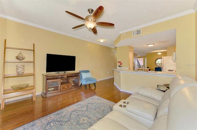 living area with wood finished floors, visible vents, ornamental molding, baseboards, and ceiling fan