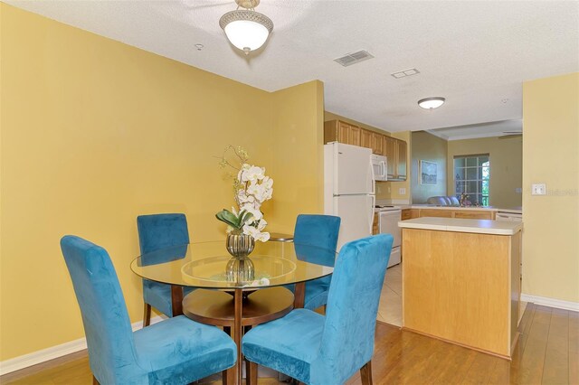 dining room with light wood-style flooring, visible vents, and a textured ceiling