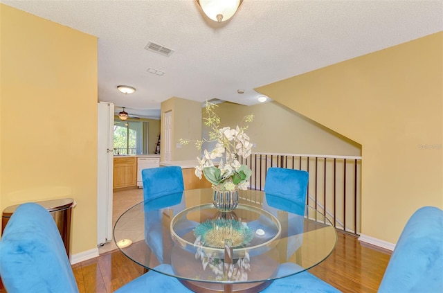 dining area featuring baseboards, light wood-style flooring, visible vents, and a textured ceiling