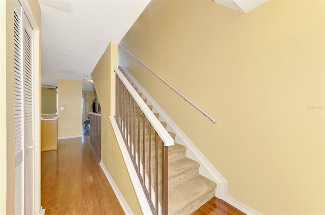 stairs featuring baseboards, wood finished floors, and a textured ceiling