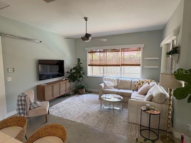 living room featuring concrete floors, a textured ceiling, baseboards, and ceiling fan