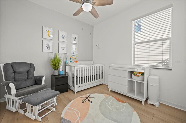 bedroom with a nursery area, baseboards, ceiling fan, and wood finished floors