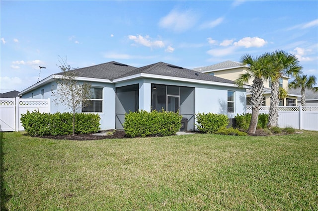 exterior space with roof with shingles, stucco siding, fence, a front lawn, and a sunroom