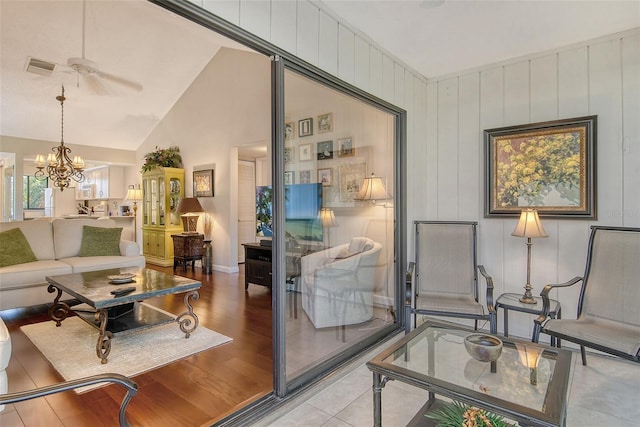 living room featuring vaulted ceiling, wood finished floors, ceiling fan with notable chandelier, baseboards, and visible vents