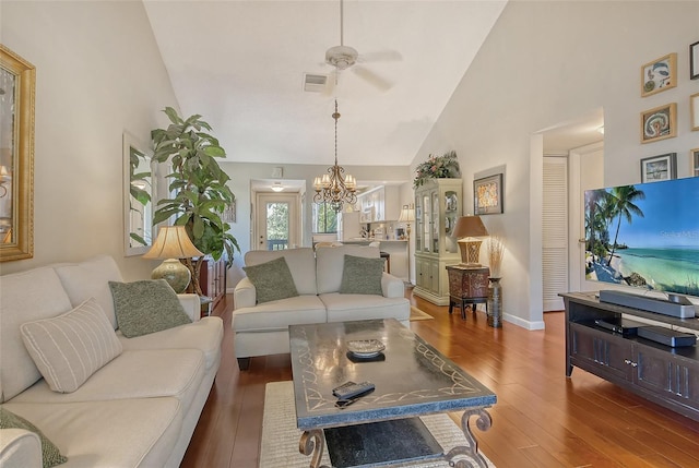 living area with high vaulted ceiling, wood finished floors, ceiling fan with notable chandelier, baseboards, and visible vents