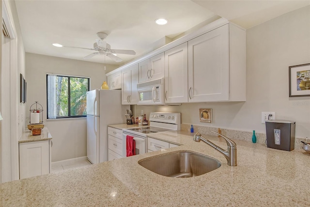 kitchen with white cabinets, a sink, a ceiling fan, white appliances, and light stone countertops