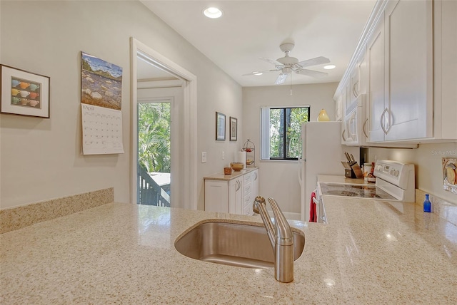 kitchen with white cabinets, a sink, white appliances, light stone countertops, and ceiling fan