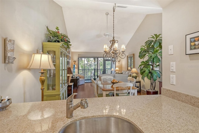 kitchen featuring high vaulted ceiling, a notable chandelier, light stone countertops, and a sink