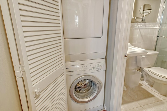washroom with stacked washer / drying machine, tile patterned floors, laundry area, and tile walls
