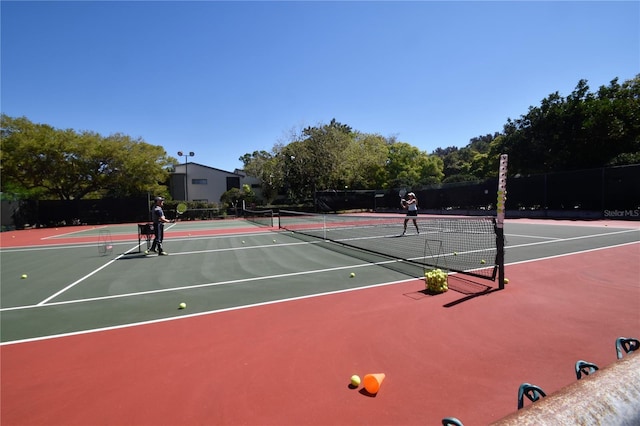 view of tennis court with community basketball court and fence