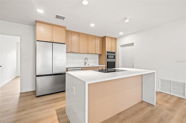 1050 55th Ave S, Saint Petersburg, FL 33705 - kitchen featuring appliances with stainless steel finishes, light countertops, a kitchen island with sink, backsplash, and light wood-type flooring