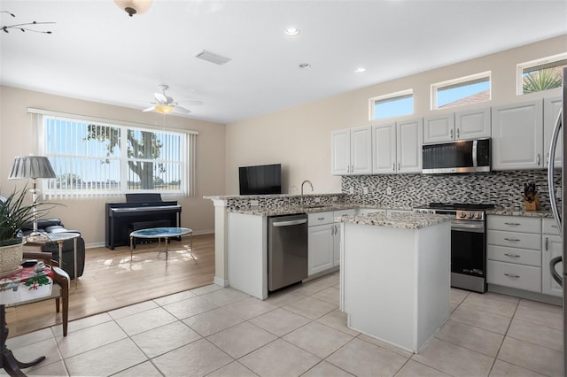 1322 Millbrook Cir, Bradenton, FL 34212 - kitchen with a peninsula, visible vents, decorative backsplash, light stone countertops, and appliances with stainless steel finishes