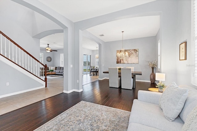 living area with hardwood / wood-style flooring, baseboards, stairs, arched walkways, and ceiling fan with notable chandelier