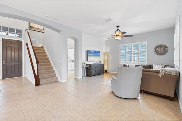 living area with light tile patterned floors, visible vents, arched walkways, ceiling fan, and stairs