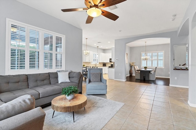 living room with arched walkways, baseboards, ceiling fan with notable chandelier, and light tile patterned flooring