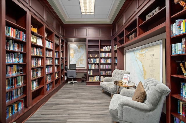 living area featuring bookshelves, light wood-style floors, ornamental molding, and built in shelves