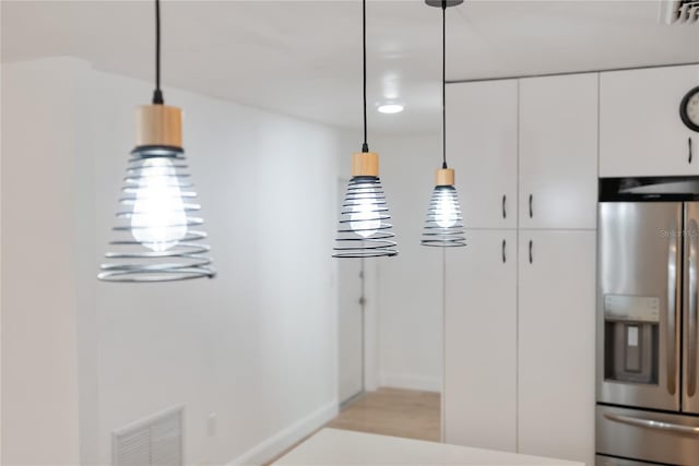 interior space featuring stainless steel fridge with ice dispenser, white cabinetry, visible vents, and hanging light fixtures