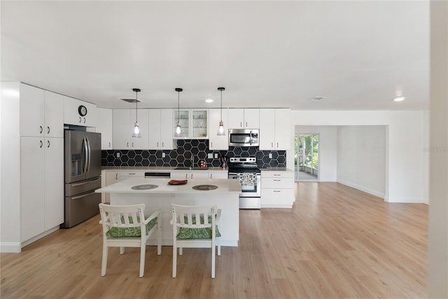 kitchen featuring tasteful backsplash, light wood-type flooring, white cabinetry, a kitchen island, and appliances with stainless steel finishes
