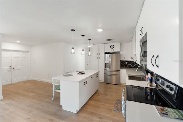 kitchen with white cabinets, a kitchen island, visible vents, a sink, and stainless steel appliances