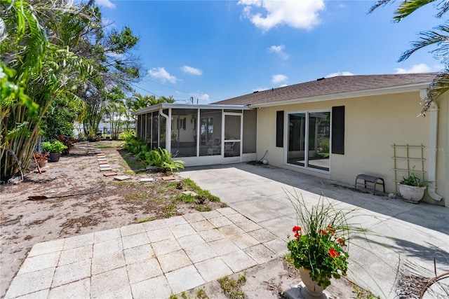 back of property featuring a shingled roof, a patio, a sunroom, and stucco siding