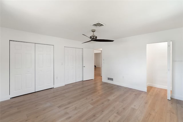 unfurnished bedroom with light wood finished floors, visible vents, baseboards, and two closets