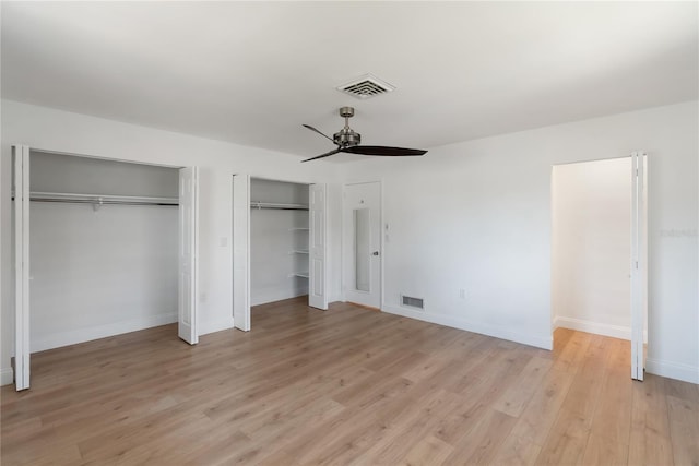 unfurnished bedroom featuring light wood finished floors, baseboards, visible vents, and multiple closets