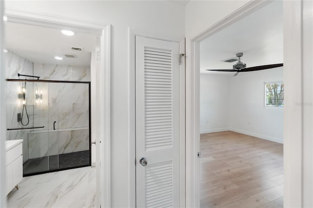 bathroom with ceiling fan, vanity, wood finished floors, a marble finish shower, and baseboards