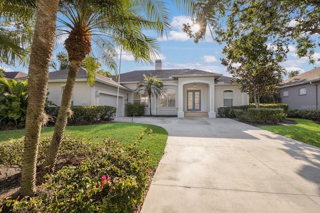 view of front of home featuring a front yard, an attached garage, concrete driveway, stucco siding, and french doors
