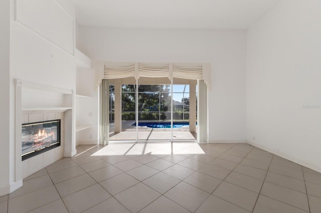 unfurnished living room with built in shelves, tile patterned flooring, a glass covered fireplace, and baseboards