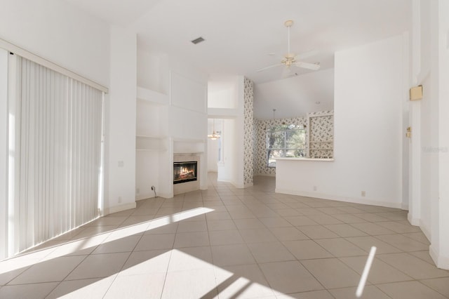 unfurnished living room with a glass covered fireplace, light tile patterned floors, a ceiling fan, visible vents, and high vaulted ceiling