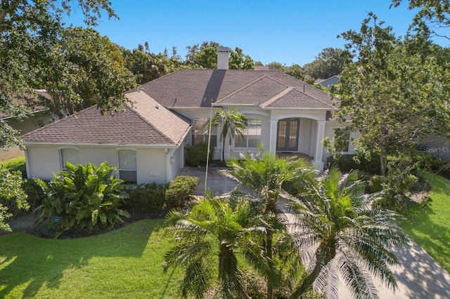 mediterranean / spanish home with a front yard, roof with shingles, a chimney, and stucco siding