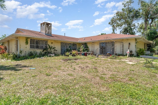 back of property featuring a lawn, stucco siding, and a chimney